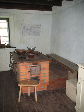 Skromno opremljena kuhinja z zidanim štedilnikom in klopjo ob steni
